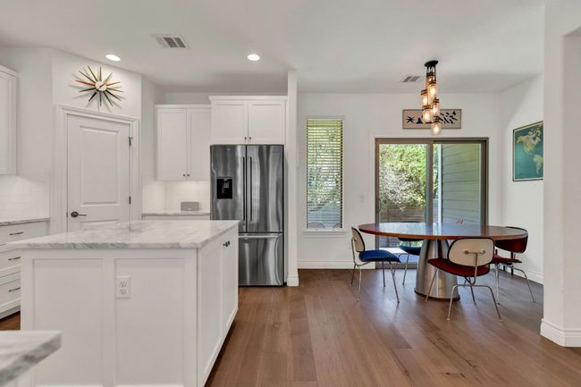 Kitchen featuring stainless steel fridge, dark wood-style flooring, white cabinets, light stone counters, and recessed lighting | Image 5