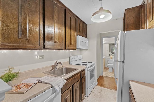 Kitchen with white appliances, a sink, dark brown cabinetry, light countertops, and hanging light fixtures | Image 8