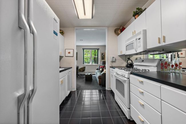 Kitchen with white appliances, white cabinetry, dark countertops, and dark tile patterned floors | Image 6