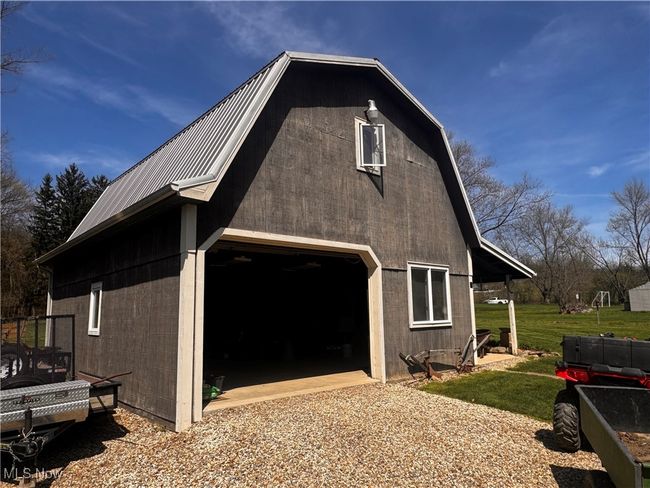 View of side of home with a barn, an outdoor structure, gravel driveway, metal roof, and a detached garage | Image 5