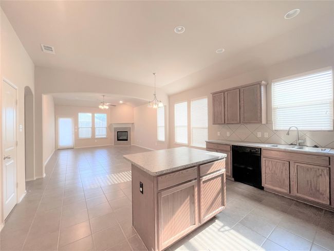 Kitchen featuring black dishwasher, light tile patterned floors, ceiling fan, backsplash, and a glass covered fireplace | Image 6