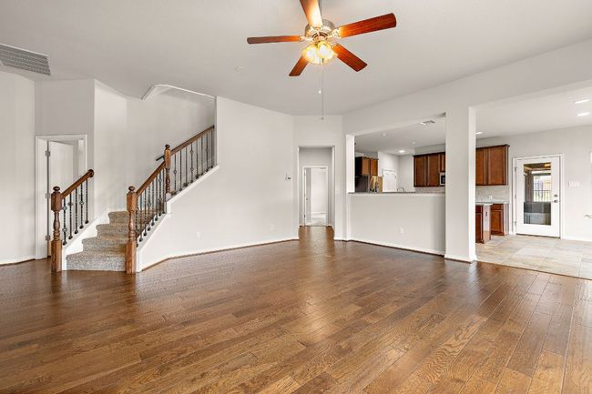 Unfurnished living room with dark wood-style floors, visible vents, baseboards, a ceiling fan, and stairs | Image 5
