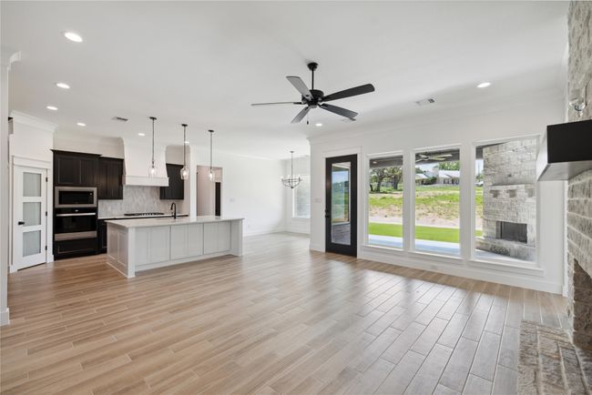 Unfurnished living room with sink, crown molding, light hardwood / wood-style flooring, a fireplace, and ceiling fan with notable chandelier | Image 12
