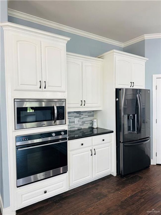 Kitchen with stainless steel appliances, dark wood-type flooring, decorative backsplash, white cabinetry, and dark countertops | Image 4