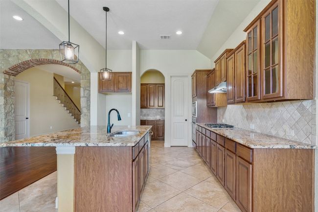 Kitchen with brown cabinets, lofted ceiling, light stone countertops, tasteful backsplash, and hanging light fixtures | Image 20