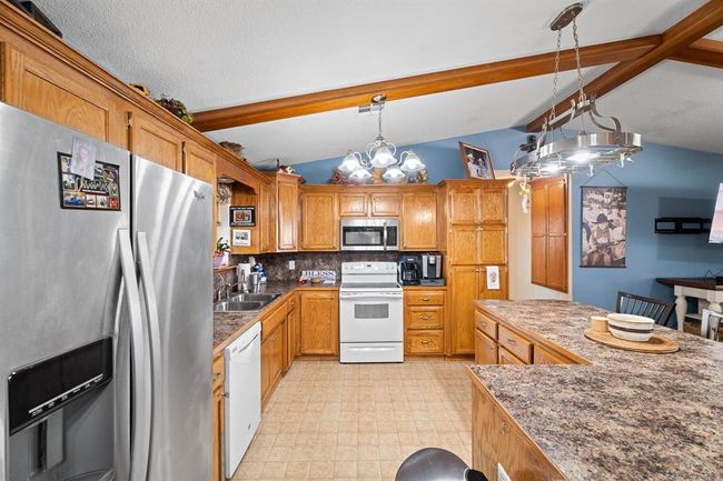 Kitchen featuring a sink, backsplash, lofted ceiling with beams, appliances with stainless steel finishes, and decorative light fixtures | Image 16