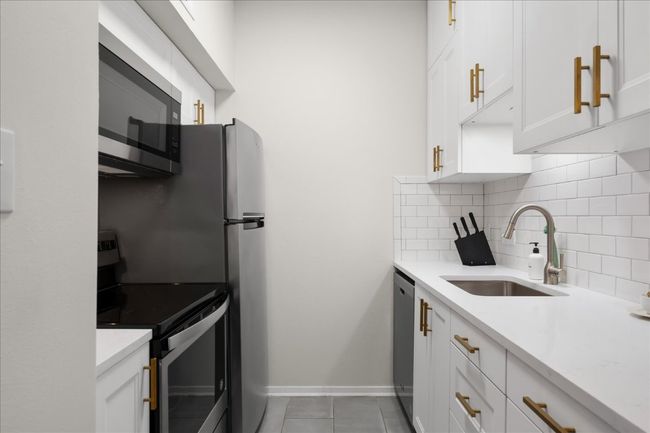 Kitchen featuring appliances with stainless steel finishes, tasteful backsplash, white cabinetry, light tile patterned flooring, and light countertops | Image 16