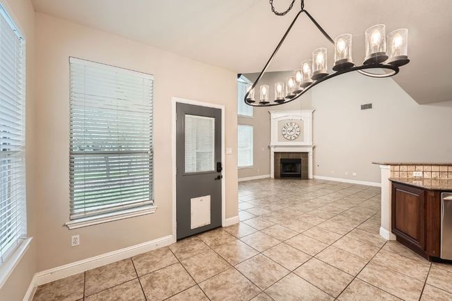 Kitchen featuring visible vents, a tiled fireplace, baseboards, a notable chandelier, and light tile patterned flooring | Image 17