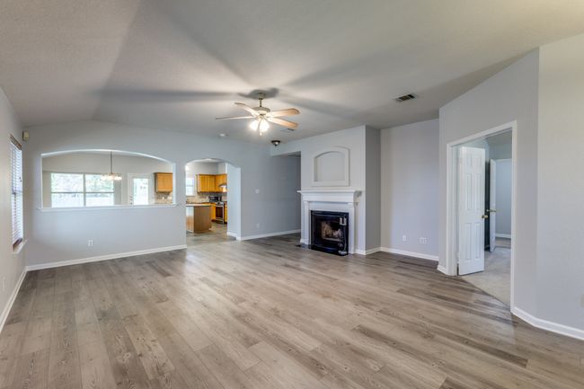 Unfurnished living room featuring a ceiling fan, arched walkways, light wood-type flooring, a fireplace with flush hearth, and vaulted ceiling | Image 8