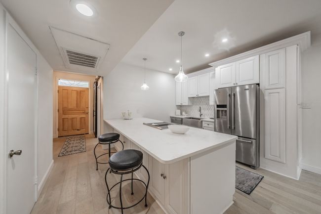 Kitchen with stainless steel fridge, light wood-style floors, visible vents, and a breakfast bar area | Image 19
