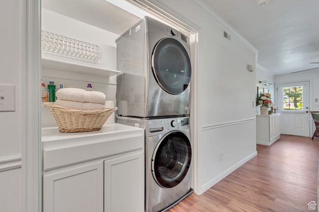 Laundry room with stacked washing machine and dryer, light wood-type flooring, crown molding, baseboards, and cabinet space | Image 7