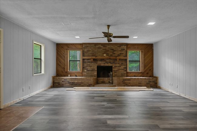 Unfurnished living room with wood finished floors, a ceiling fan, a textured ceiling, a fireplace, and wood walls | Image 24