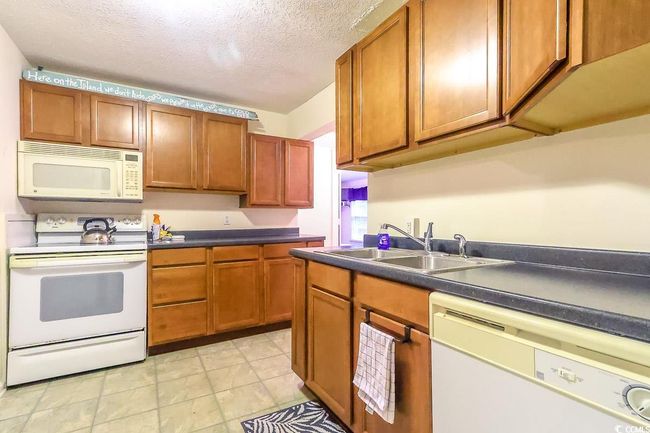Kitchen featuring white appliances, dark countertops, a textured ceiling, brown cabinets, and light tile patterned floors | Image 7