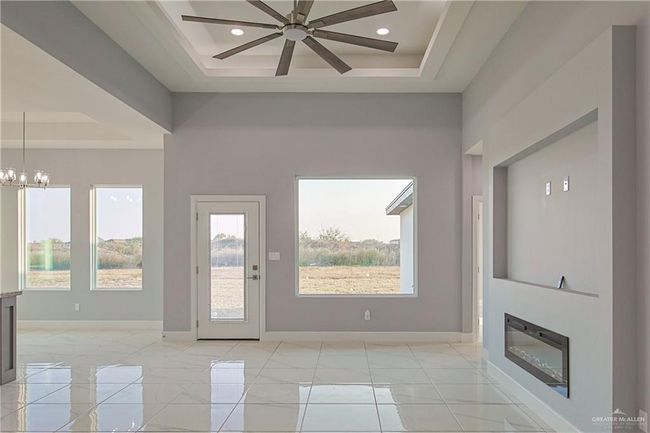 Unfurnished living room featuring ceiling fan with notable chandelier and a raised ceiling | Image 6