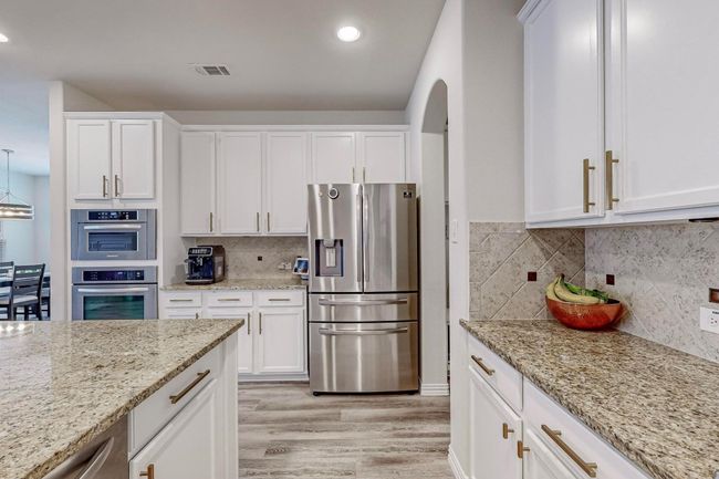 Kitchen with stainless steel appliances, light wood-style floors, white cabinets, light stone counters, and recessed lighting | Image 23