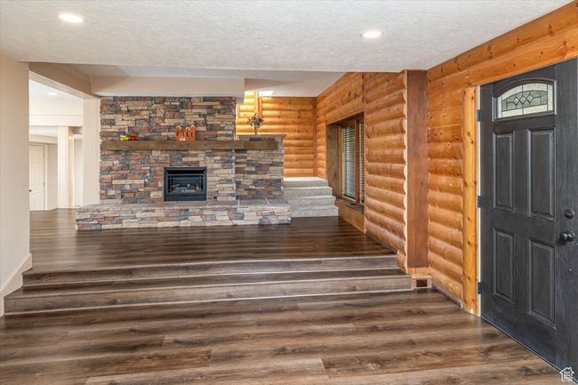 Unfurnished living room with log walls, a textured ceiling, wood finished floors, a stone fireplace, and recessed lighting | Image 24