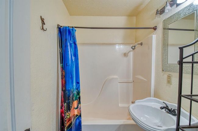 Full bathroom featuring a textured wall, a sink, shower / bathtub combination with curtain, and a textured ceiling | Image 16