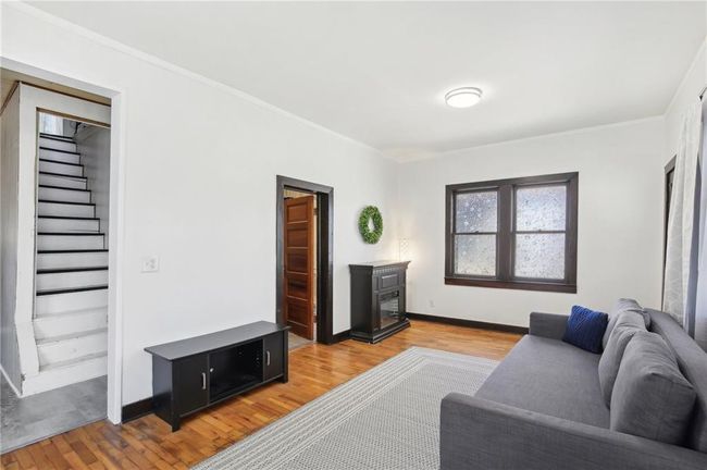 Living area featuring light wood-type flooring, crown molding, baseboards, a fireplace, and stairs | Image 7
