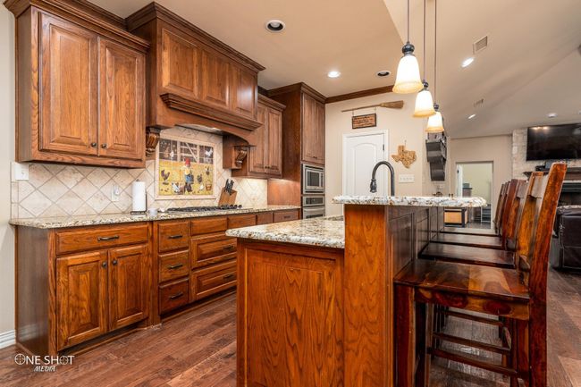 Kitchen featuring appliances with stainless steel finishes, dark wood finished floors, light stone countertops, tasteful backsplash, and recessed lighting | Image 12