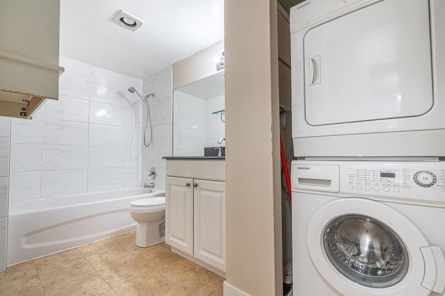 Bathroom with vanity, stacked washer and clothes dryer, bathing tub / shower combination, tile patterned flooring, and toilet | Image 20