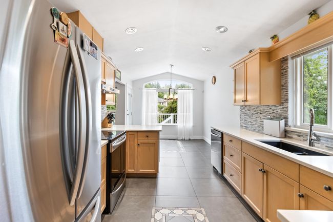 Kitchen featuring stainless steel appliances, a sink, vaulted ceiling, plenty of natural light, and light countertops | Image 7