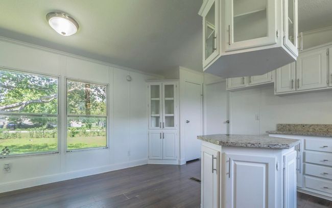 Kitchen featuring dark wood finished floors, crown molding, glass insert cabinets, white cabinetry, and a center island | Image 4