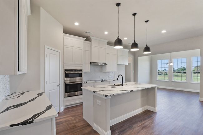 Kitchen with tasteful backsplash, white cabinets, black electric cooktop, dark wood finished floors, and double oven | Image 4