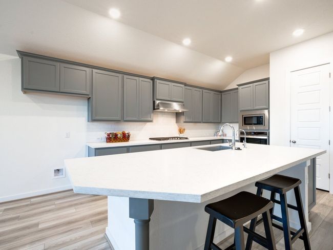 Kitchen with gray cabinets, decorative backsplash, exhaust hood, light countertops, and lofted ceiling | Image 17