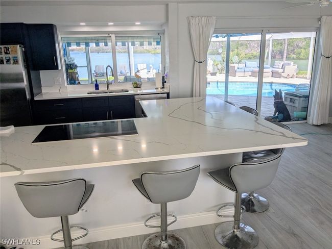 Kitchen featuring a kitchen bar, appliances with stainless steel finishes, a sink, dark cabinets, and light stone counters | Image 18