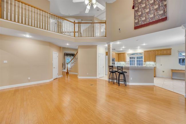 Living room featuring ornate columns, ceiling fan, light wood-type flooring, stairway, and a towering ceiling | Image 13