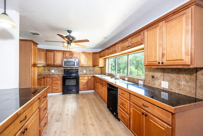 Kitchen featuring tasteful backsplash, visible vents, a ceiling fan, black appliances, and light wood-style flooring | Image 9