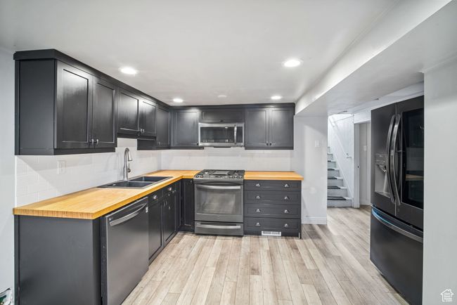 Kitchen featuring appliances with stainless steel finishes, a sink, wooden counters, light wood-style flooring, and backsplash | Image 14