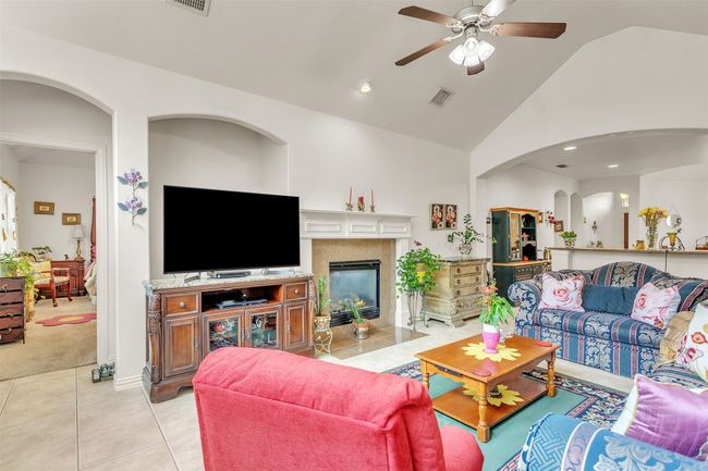 Living area featuring ceiling fan, light tile patterned flooring, light colored carpet, a fireplace, and arched walkways | Image 20