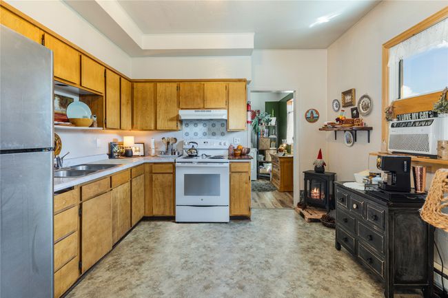 Kitchen featuring freestanding refrigerator, open shelves, white electric stove, under cabinet range hood, and a sink | Image 12