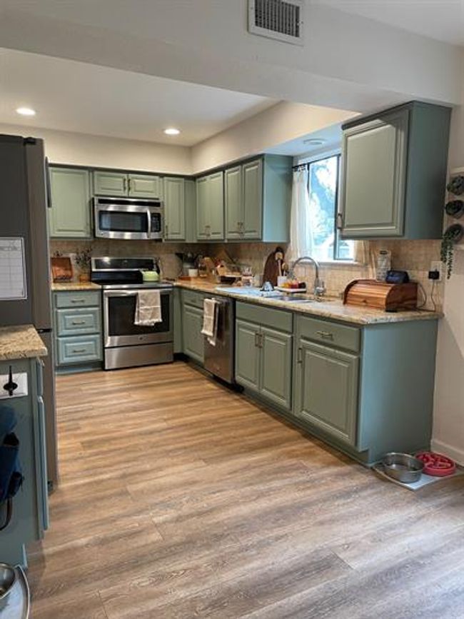 Kitchen featuring stainless steel appliances, green cabinets, light wood-style floors, a sink, and backsplash | Image 4
