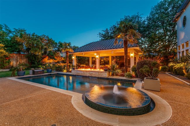 The circular spa has a pretty fountain feature, and begins your entrance into the backyard retreat. Lots of lush tropical-style landscaping, the impressive view of the tile-topped patio area and perfectly placed lighting set the mood for the evening. | Image 34