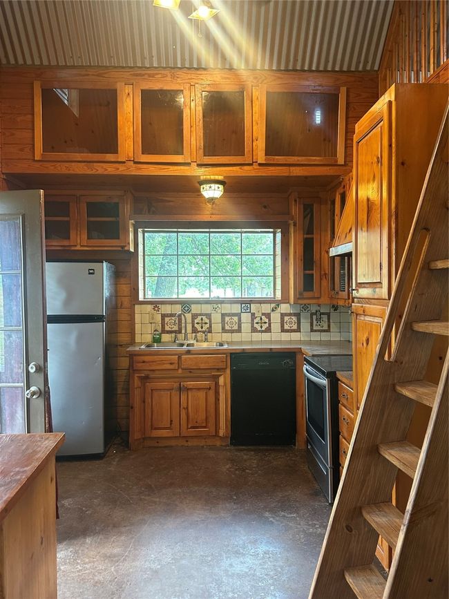 Kitchen featuring dishwashing machine, refrigerator, stove, a sink, and concrete flooring | Image 6