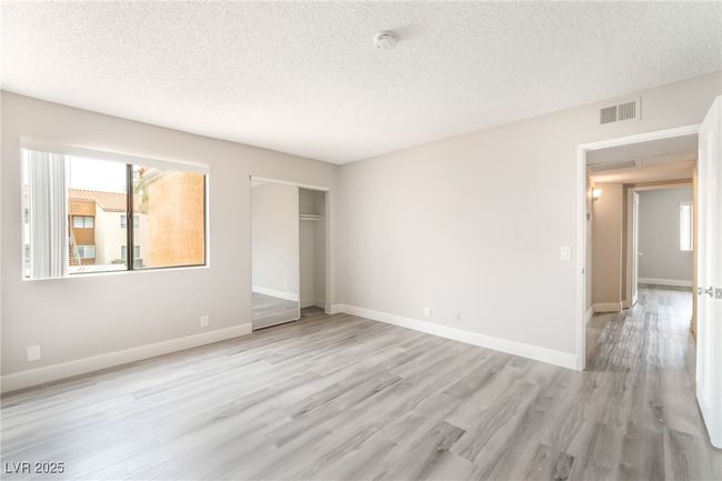 Unfurnished bedroom with a textured ceiling, multiple windows, light wood-style flooring, and a closet | Image 15