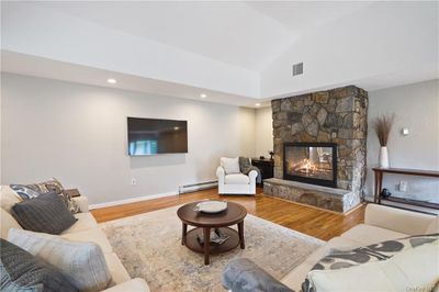 Living room featuring a stone fireplace, wood-type flooring, lofted ceiling, and a baseboard heating unit | Image 2