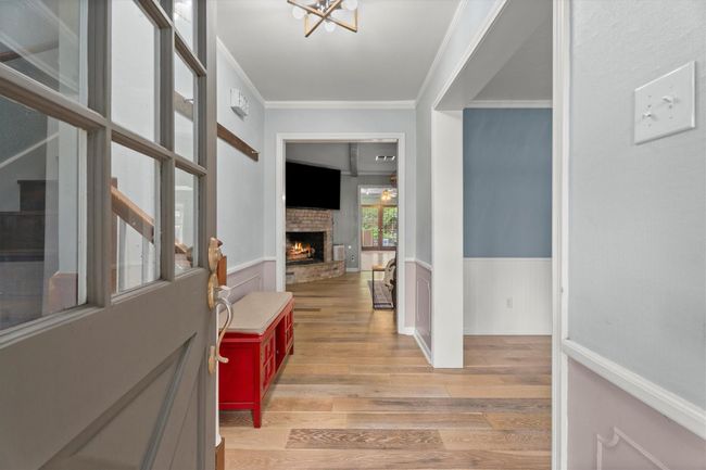 This welcoming entryway features beautiful flooring, a bright open layout, and a cozy view of the living room with a fireplace. Formal dining is directly to the right and staircase is on the left side, leading to the secondary bedrooms. | Image 5