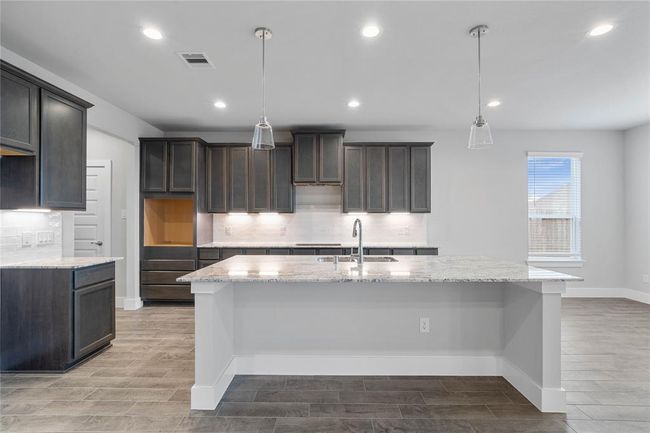 This kitchen is by far any chef’s dream! This spacious kitchen features high ceilings, stained wood cabinets, granite countertops, SS appliances, modern tile backsplash, recessed and pendant lighting, extended counter space, granite kitchen island with space for breakfast bar, and a walk-in pantry all overlooking your huge family room. | Image 8