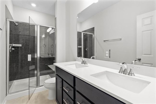 This primary bathroom is definitely move-in ready! Featuring an oversized walk in shower with seat and tile surround, stained cabinets with light countertops, dual vanities, framed mirrow, high ceilings, custom paint, sleek and modern finishes. | Image 12