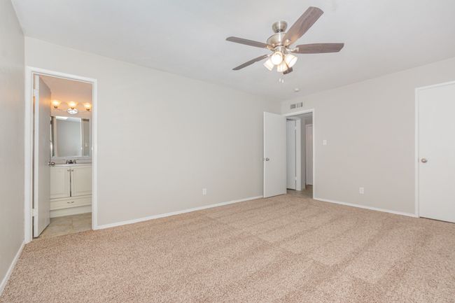 Unfurnished bedroom featuring light carpet, ensuite bathroom, and a ceiling fan | Image 15