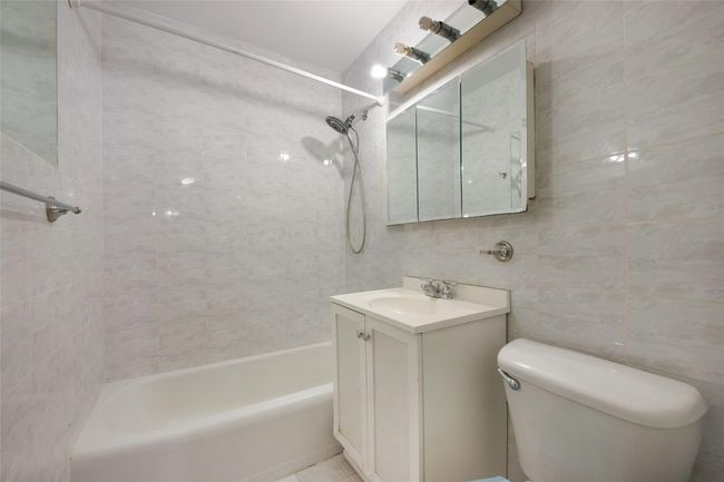 Full bathroom featuring tiled shower / bath combo, tile patterned flooring, toilet, tile walls, and vanity | Image 9
