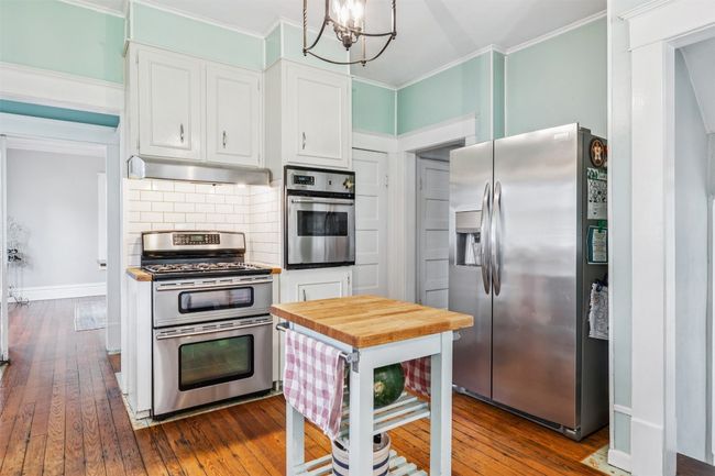 Kitchen with stainless steel appliances, under cabinet range hood, dark wood finished floors, white cabinets, and ornamental molding | Image 14