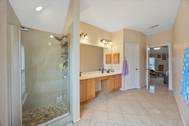 Bathroom with double vanity, a shower stall, tile patterned floors, and baseboards | Image 30