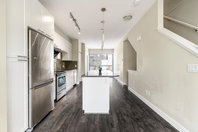 Kitchen featuring dark wood-style floors, appliances with stainless steel finishes, decorative backsplash, and white cabinetry | Image 8