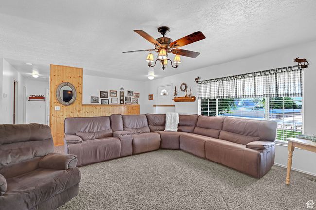 Living area featuring wood walls, a textured ceiling, ceiling fan, and carpet | Image 5