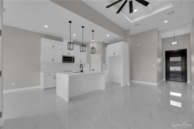 Kitchen with ceiling fan, white cabinets, light tile patterned flooring, decorative light fixtures, and an island with sink | Image 3