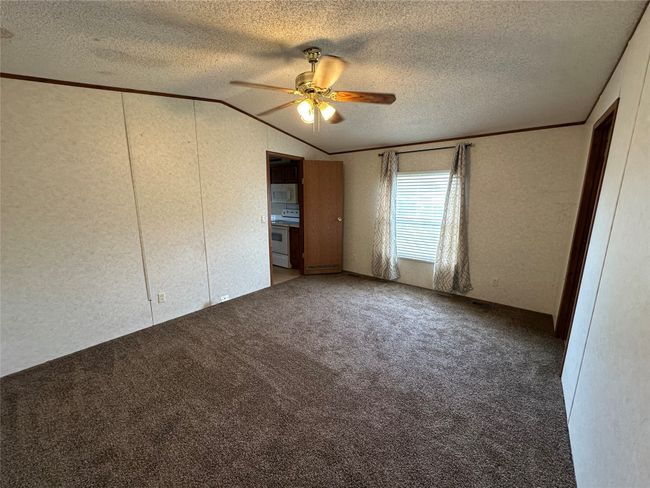 Unfurnished bedroom with lofted ceiling, a textured ceiling, carpet floors, a textured wall, and a ceiling fan | Image 19